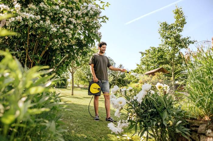 Mężczyzna podlewa trawę i rośliny wężem ogrodowym